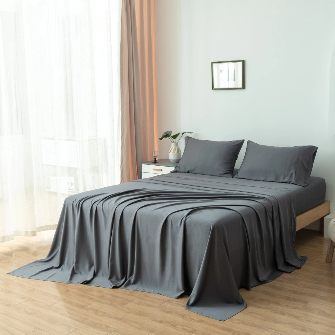 A neatly made bed with Linenly's granite grey Bamboo Pillowcase Set in a serene bedroom with minimal decor and sheer curtains draping the window.