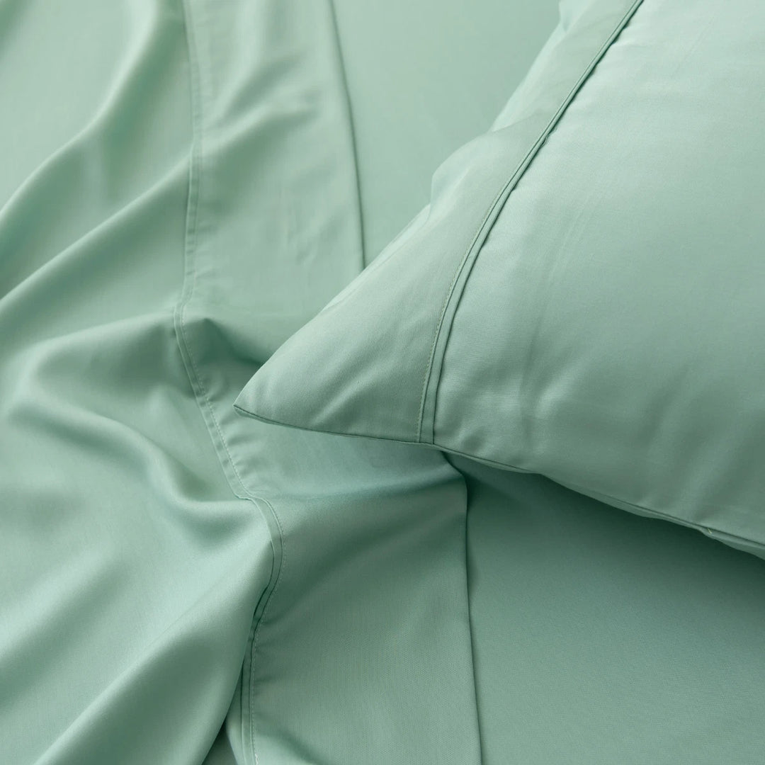 Close-up of a Linenly Green Sheen Bamboo Pillowcase Set and a hypoallergenic organic bamboo pillow, with an emphasis on the fabric's texture and the cozy, inviting arrangement.