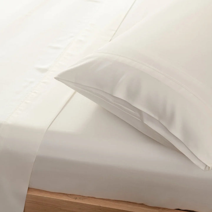 A close-up view of a neatly made bed with crisp white sheets and Linenly organic bamboo pillowcases in Ivory, showcasing a clean and simple bedroom aesthetic.