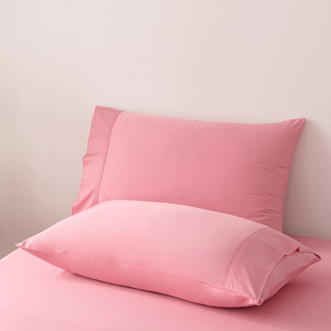A soft pink Linenly bamboo pillowcase set in Light Rose, propped against a wall on a matching pink surface, suggesting a serene and hypoallergenic sleep atmosphere.
