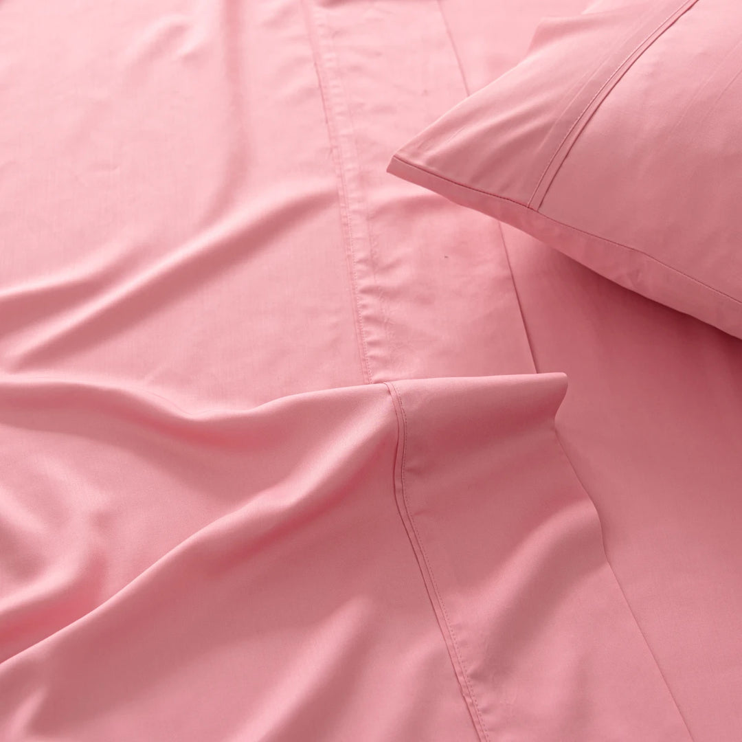 Soft pink bedding with a close-up view of a neatly made bed showcasing a smooth duvet and Linenly's Light Rose Bamboo Pillowcase Set.