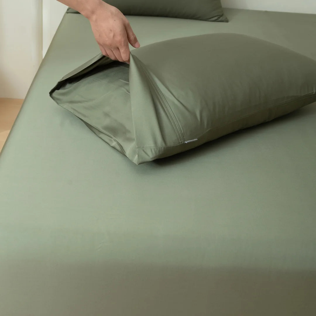 A hand smoothens a Linenly Bamboo Pillowcase Set in Moss over a pillow on a neatly made bed with matching bed linens.
