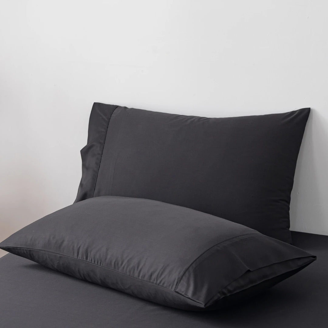 Two Linenly black bamboo pillowcases on a grey surface against a white background, offering luxury comfort.