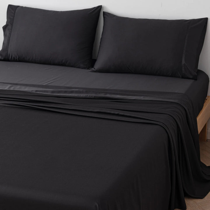 A neatly made bed with black bedding, including a fitted sheet, a flat sheet, and two pillows with Linenly's Bamboo Pillowcase Set - Black against a white wall.