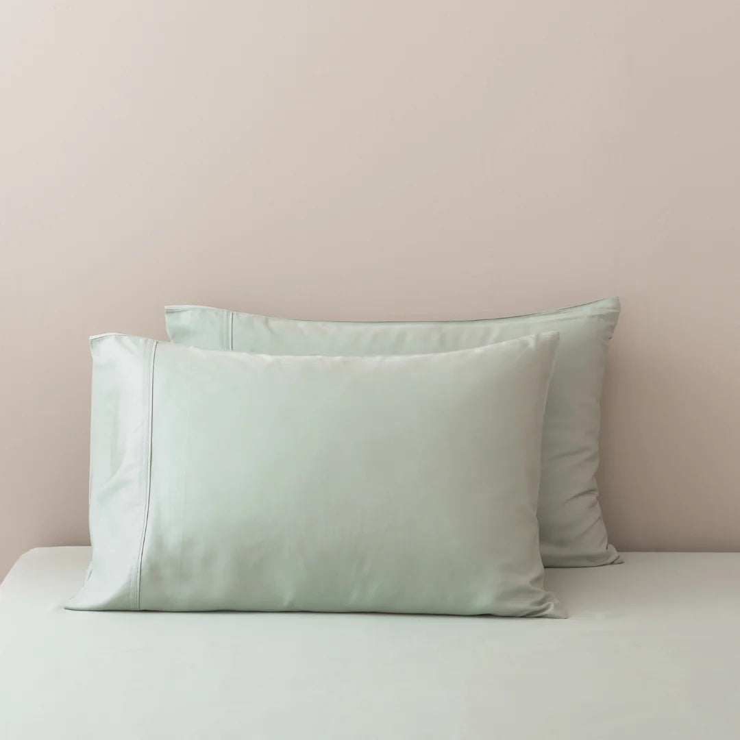 A serene setting with a pastel theme showcasing two soft pillows with Linenly Bamboo Pillowcase Set - Sage against a gently colored wall, evoking a sense of calm and relaxation.