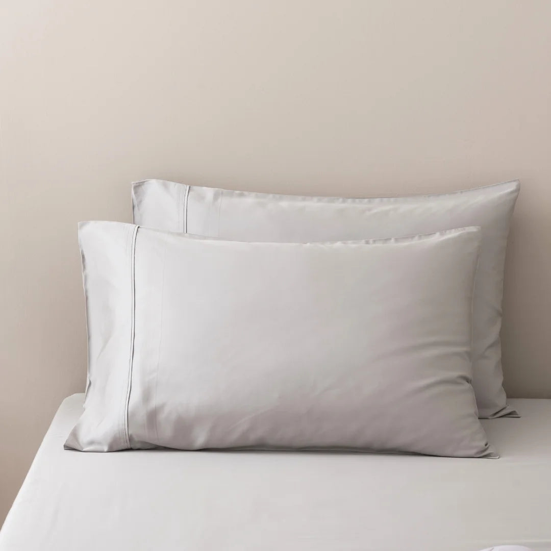 Two plush pillows on a neatly made bed with Linenly's Silver Bamboo Pillowcase Set, evoking a feeling of comfort and elegance.
