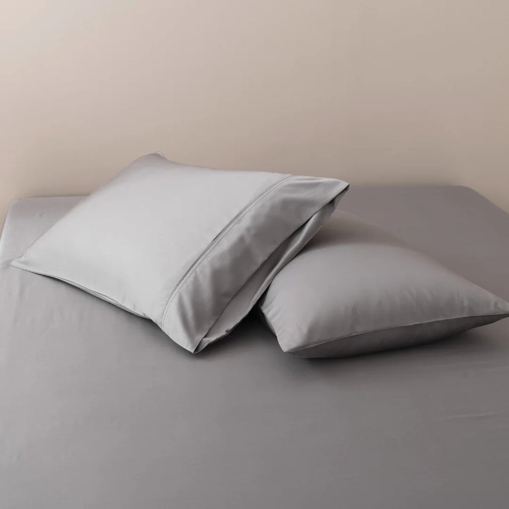 Two plush pillows with Linenly Bamboo Pillowcase Sets in Stone Grey on a neatly made bed with a smooth gray satin weave bedsheet.