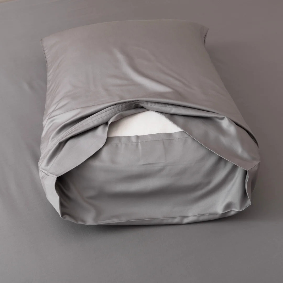 A partially unfolded Linenly bamboo pillowcase set in Stone Grey satin weave on a gray background.