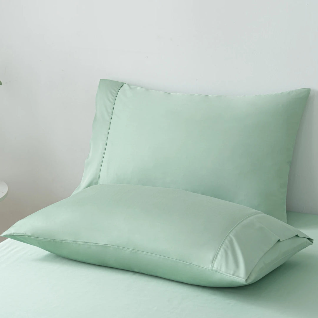 Two soft mint green pillows with Linenly Bamboo Pillowcase Set - Summer Green on a matching bedsheet set against a white wall, creating a serene and cozy bedroom atmosphere.