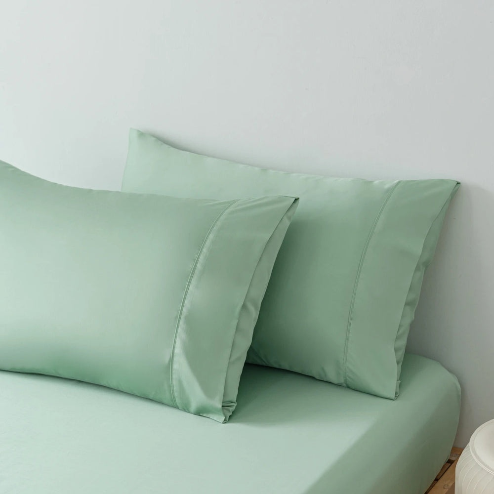 A set of smooth, Summer Green satin pillowcases made from organic bamboo on matching bed sheets from Linenly, giving a luxurious and cohesive look to the bedding.