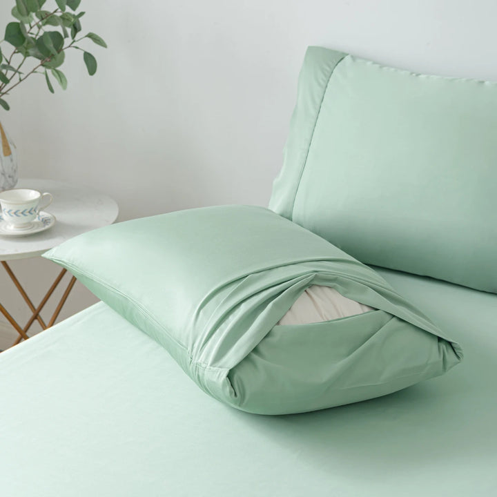 A neatly made bed with light green bed linen and a pillow partially covered with Linenly organic bamboo pillowcases in the Bamboo Pillowcase Set - Summer Green.
