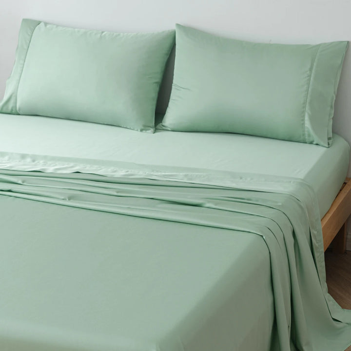 A neatly made bed with smooth, light green satin weave sheets and two matching pillows covered in Linenly's Summer Green Bamboo Pillowcase Set.