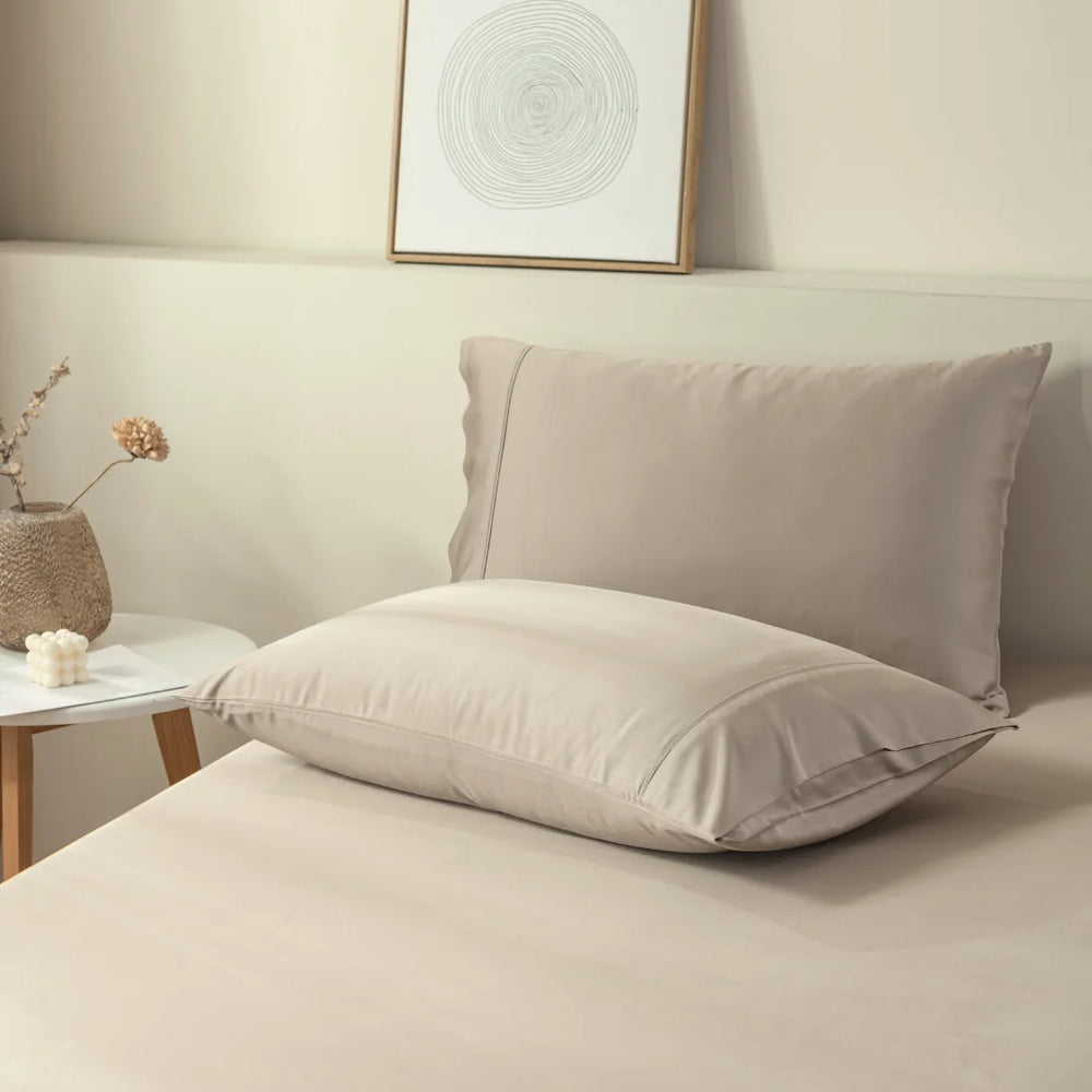 A minimalist bedroom with a neatly made bed in neutral colors, featuring a comfortable beige pillow encased in Linenly bamboo pillowcases on crisp, clean bedding, exuding a sense of calm and simplicity.