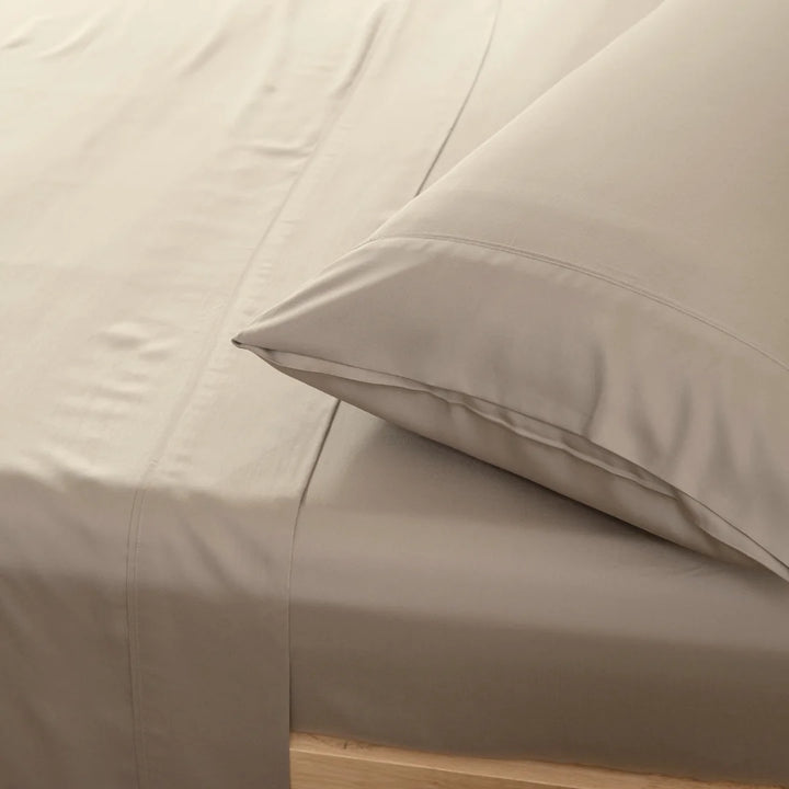 A close-up of a neatly made bed with soft beige sheets and Linenly's Bamboo Pillowcase Set in Taupe, inviting a peaceful and comfortable rest.
