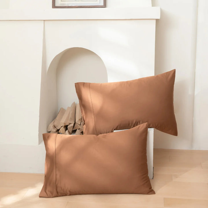 Three plush brown pillows with Linenly's Bamboo Pillowcase Set in Terracotta leaned against a white fireplace, offering a cozy and warm home decor aesthetic.