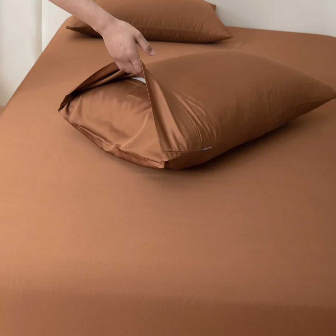 A person smoothing out luxurious Linenly bamboo pillowcases in terracotta on a neatly made bed.