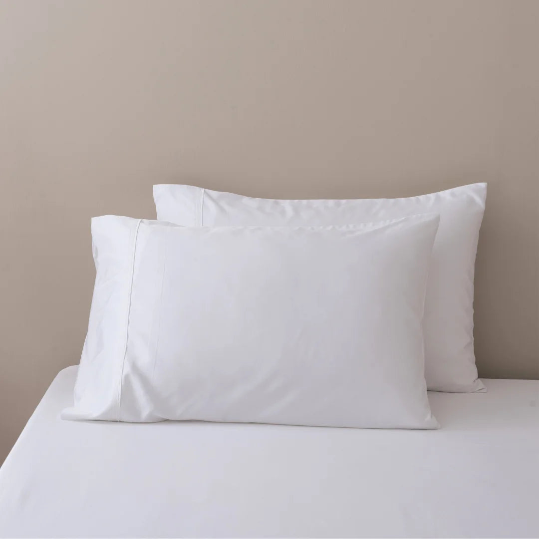 A minimalist bedroom setting with Linenly's crisp white Bamboo Pillowcase Set on a neatly made bed, against a soft beige wall.