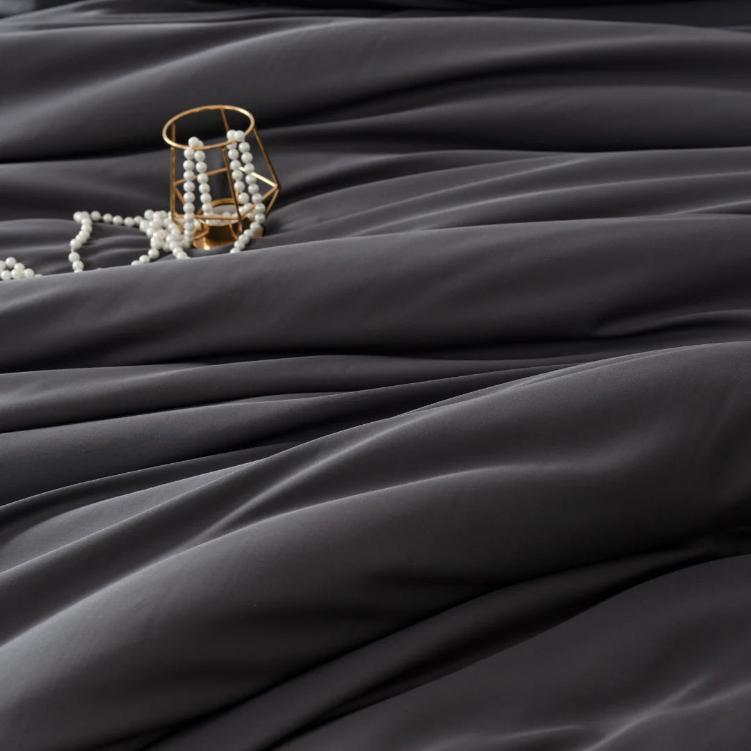 An elegant piece of jewelry resting on the luxurious folds of an Linenly Bamboo Quilt Cover - Charcoal, made from eco-friendly, dark satin fabric.