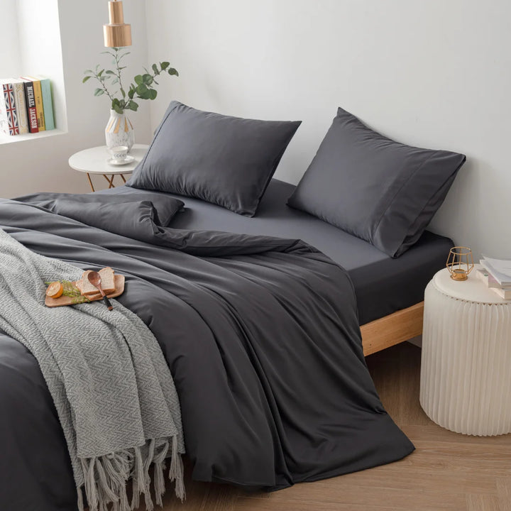 A neatly arranged bedroom with a modern minimalist aesthetic, featuring a bed with Linenly's Bamboo Quilt Cover in Charcoal and pillows, complemented by a cozy gray throw blanket at the foot of the bed.