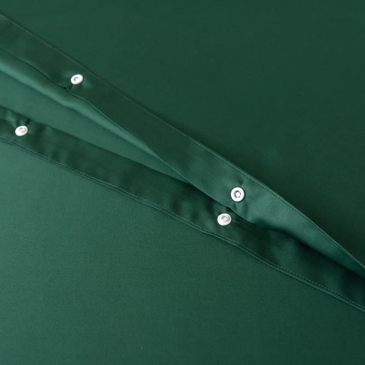 Close-up of green fabric from the Bamboo Quilt Cover Set - Evergreen by Linenly, showcasing two visible layers with rows of white buttons. The silky texture looks smooth and shiny, suggesting a luxurious satin-like finish.