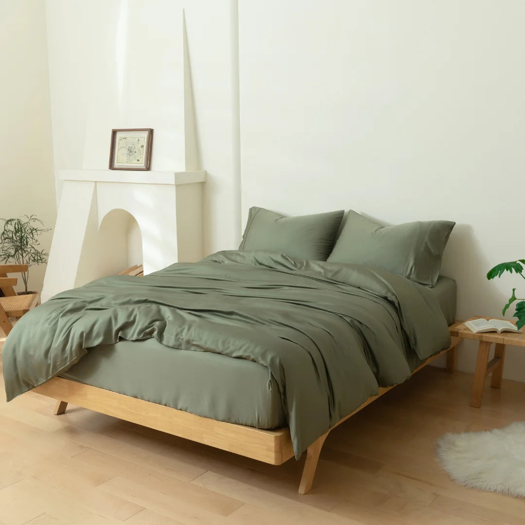 Minimalist bedroom with a neatly made bed covered in a Linenly Moss Bamboo Quilt Cover, wooden frame, and simple decor, evoking a serene and clean aesthetic.