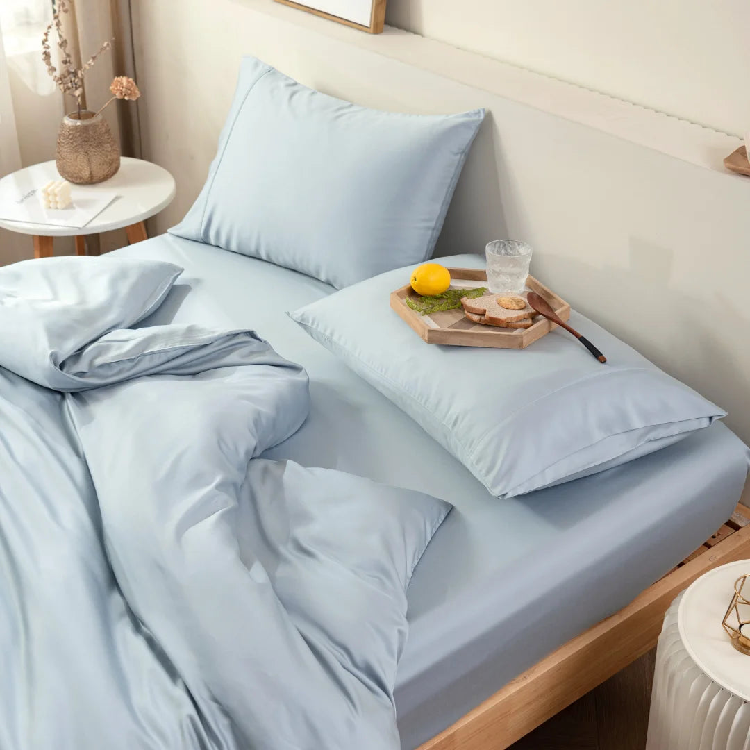 A neatly made bed with a Linenly pale blue bamboo quilt cover, featuring a wooden tray with a light breakfast and a glass of water, creating a serene and cozy morning atmosphere.