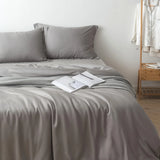 A serene bedroom with a neatly made bed adorned with a Linenly stone grey bamboo quilt cover, an open book resting in the middle, inviting a peaceful reading session, with a white shirt hanging casually in the background.