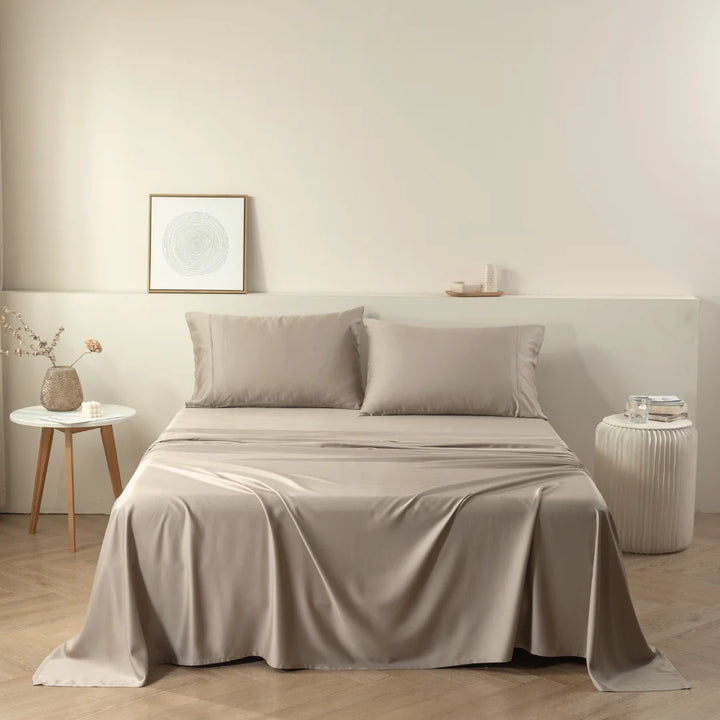 A neatly made bed with a Linenly Taupe Bamboo Quilt Cover in a minimalistic bedroom setting, accented by a small side table, decorative vase, and framed wall art, invoking a sense of calm.