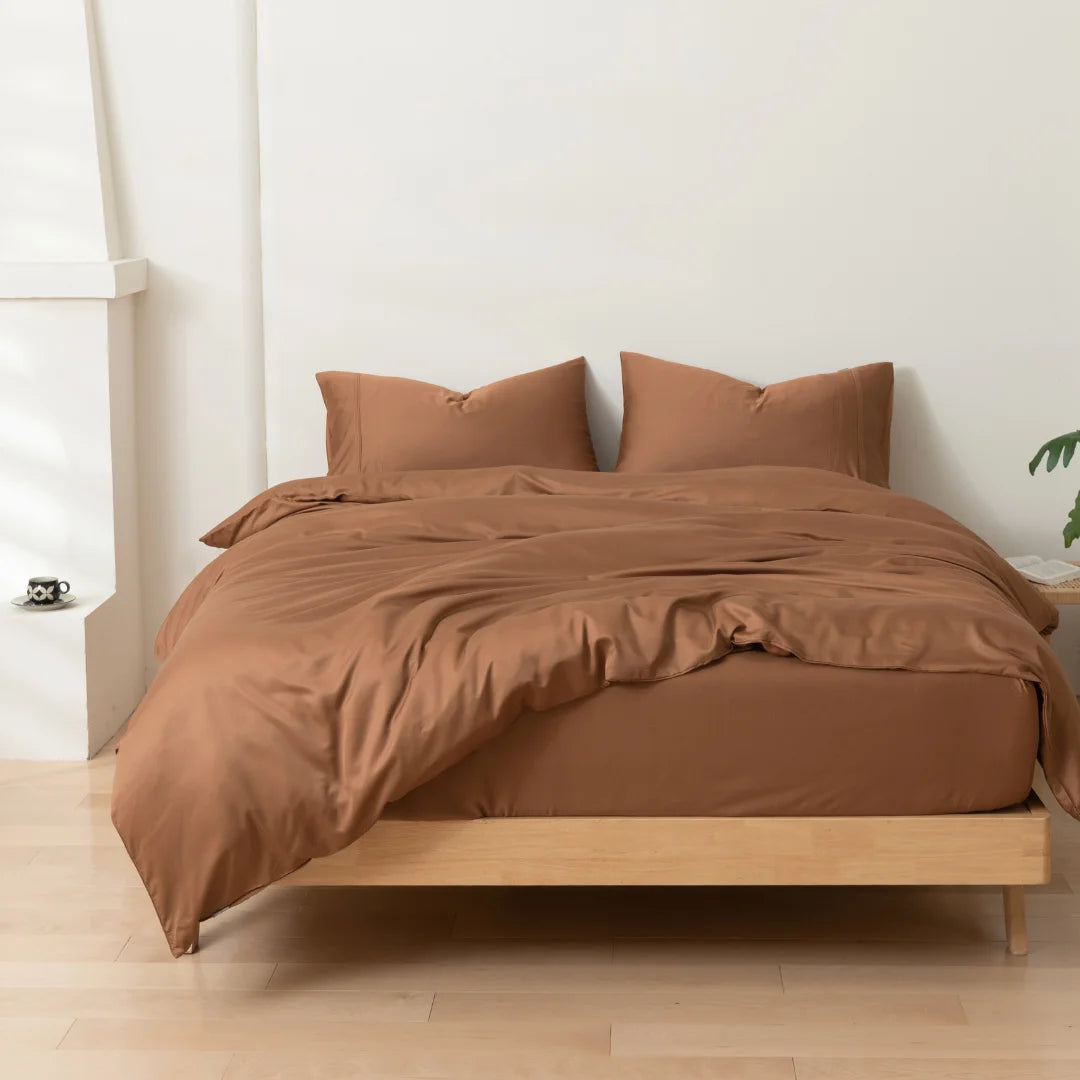 A neatly made bed with a smooth Linenly Terracotta Bamboo Quilt Cover and matching pillows in a serene bedroom setting, showcasing both comfort and style.