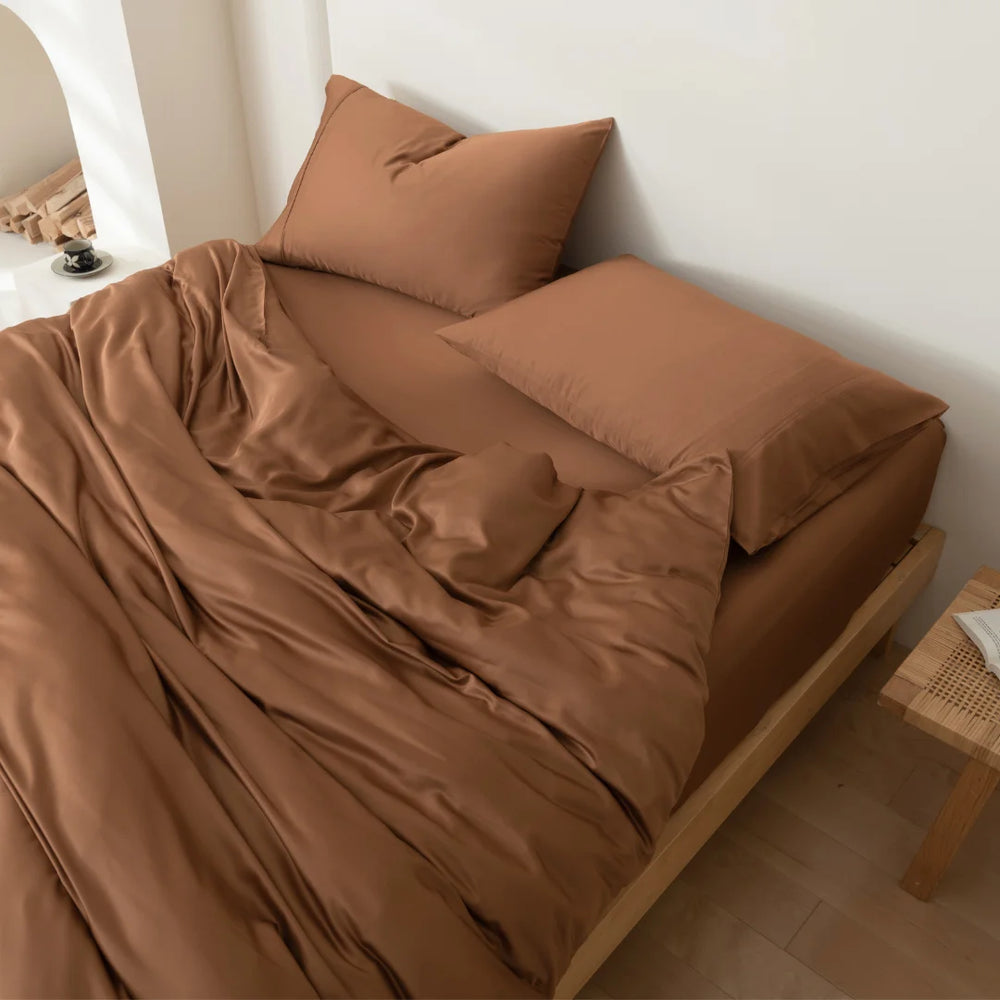 A neatly made bed with a Linenly terracotta bamboo quilt cover in a room with minimalistic decor, illustrating both luxury bedding and environmentally friendly choices.