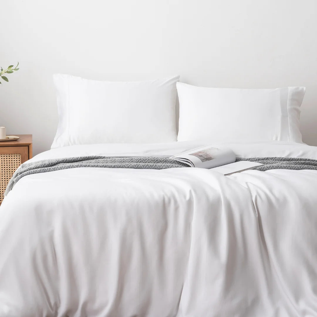 A neatly made bed with a crisp white Linenly bamboo quilt cover, an open magazine resting at the center, inviting relaxation in a minimalistic bedroom setting.
