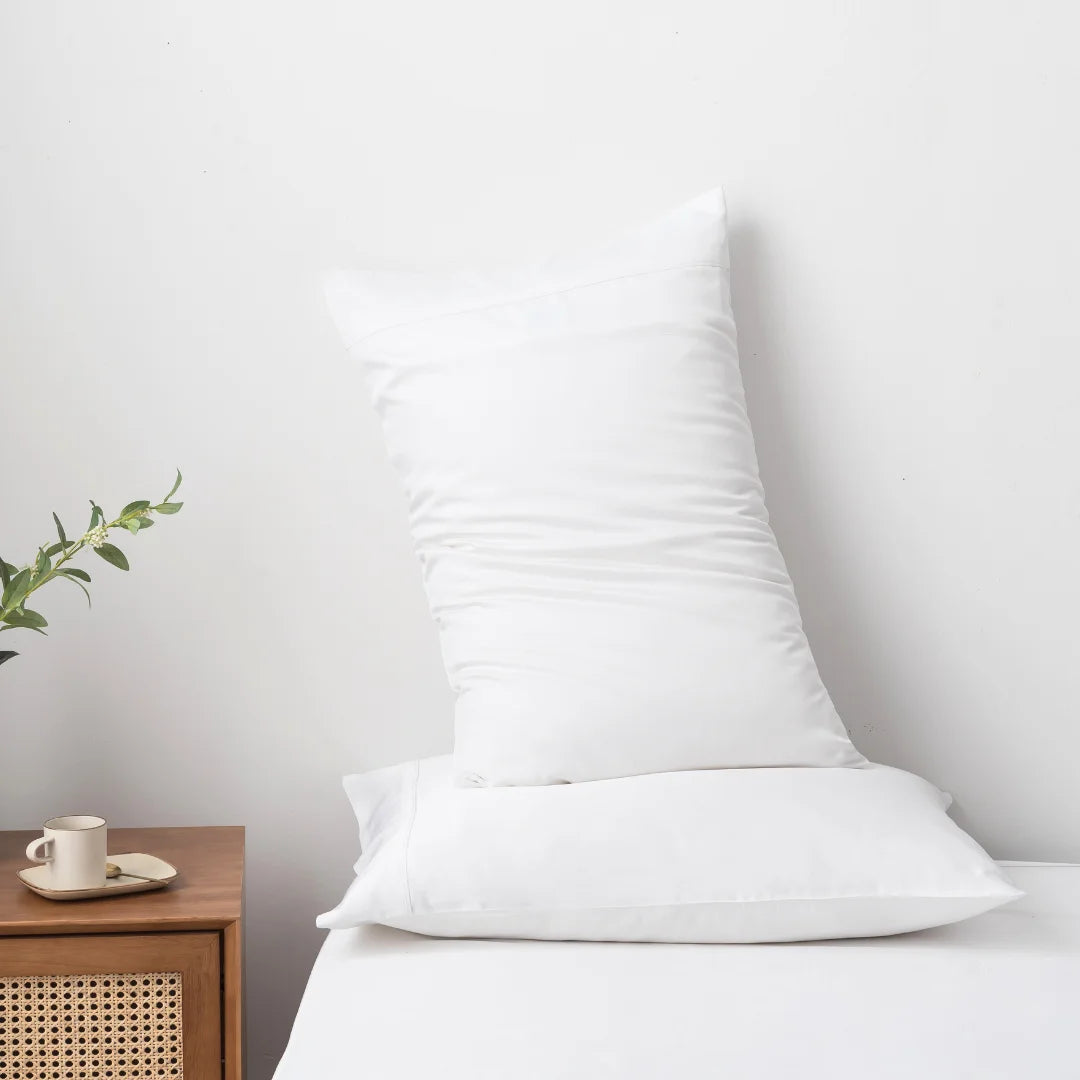 A pristine white Linenly bamboo quilt cover adorns the body pillow, which stands vertically on a neatly made bed with a wooden side table, holding a warm cup and a small green plant accessory, evoking a