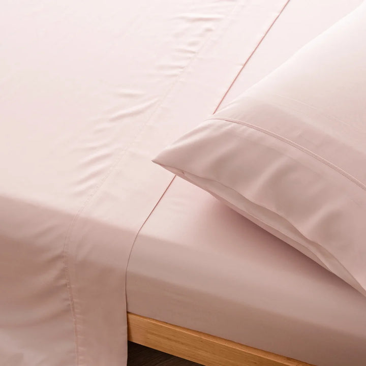 Close-up of a neatly made bed with Linenly's Bamboo Sheet Set in Blush and a pillow, highlighting comfortable and clean bedding for a breathable sleeping experience.
