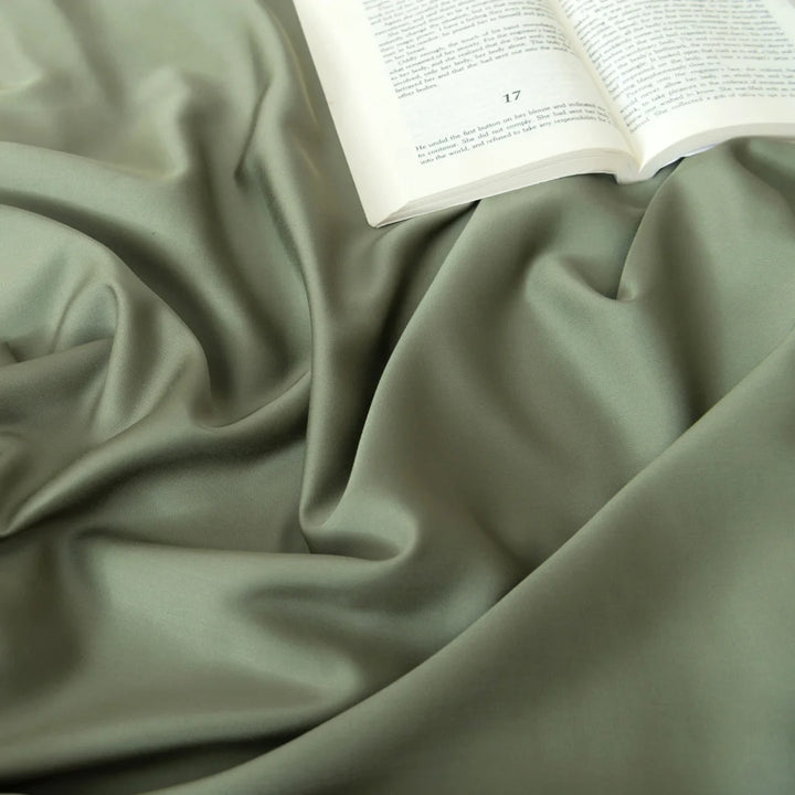 An open book nestled on Linenly's luxurious, environmentally friendly Bamboo Sheet Set in Moss fabric, creating an elegant and tranquil reading atmosphere.