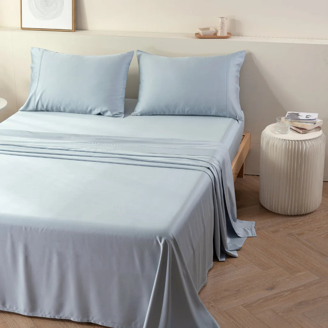 A neatly made bed with a breathable Linenly bamboo sheet set in pale blue, in a tidy bedroom, evoking a sense of calm and comfort.