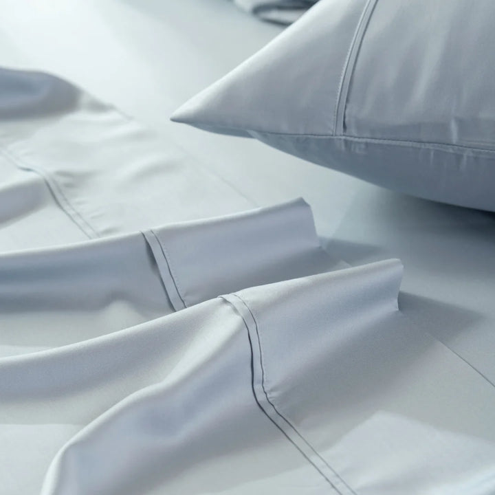 Luxurious gray satin bedding with a focus on the delicate stitching and the plush pillow, inviting a peaceful and comfortable sleep. This Linenly Bamboo Sheet Set in Pale Blue incorporates sustainable practices, ensuring both luxury and environmentally conscious design.