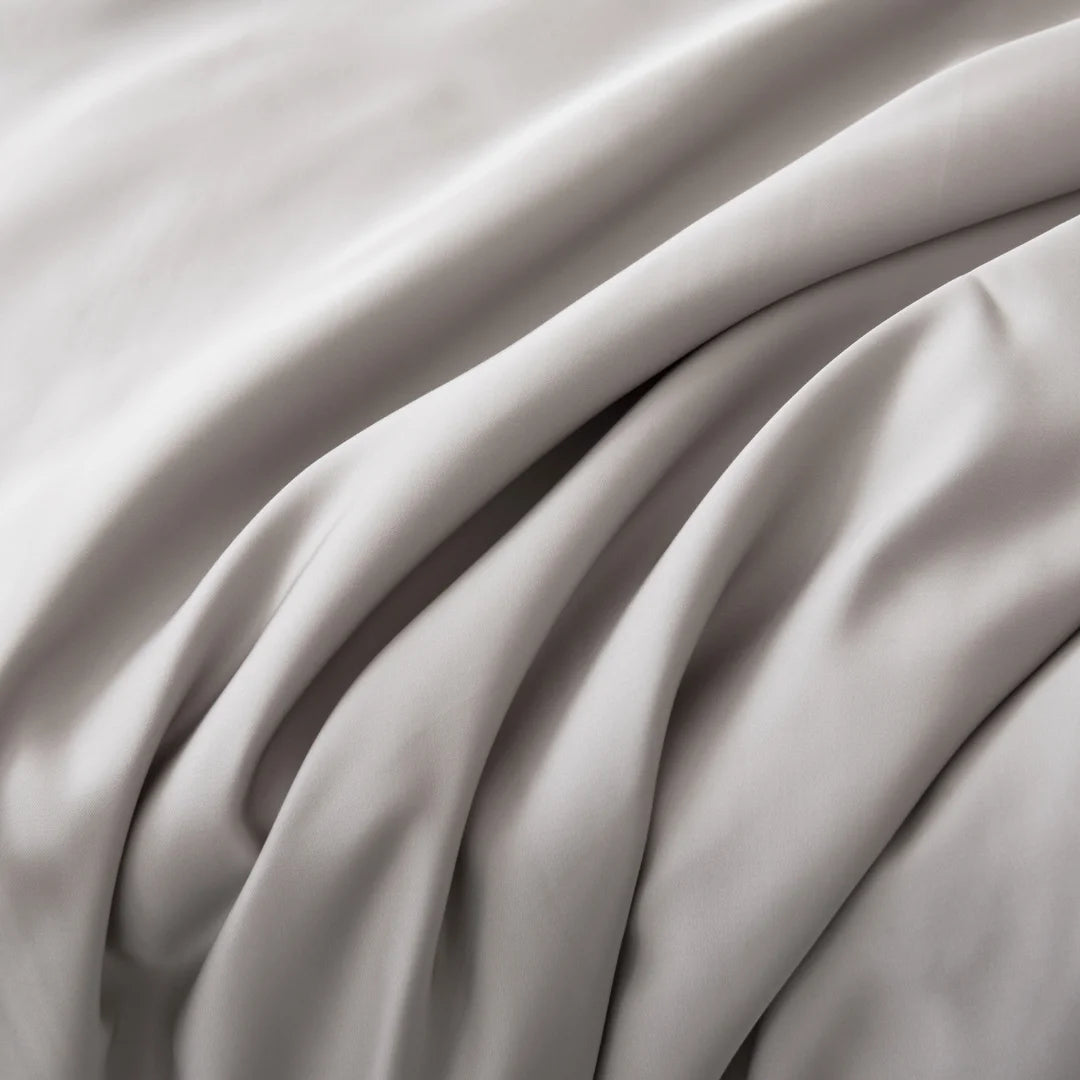 An elegant expanse of smooth, draped satin fabric in a soft, monochromatic color palette, introducing the Linenly Silver Bamboo Sheet Set.