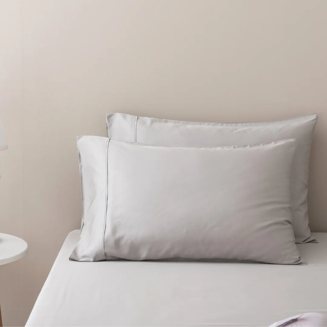 Two soft pillows on a neatly made bed with crisp white Linenly luxury Silver bamboo sheet set and a neutral-toned wall in the background, evoking a serene and comfortable atmosphere.