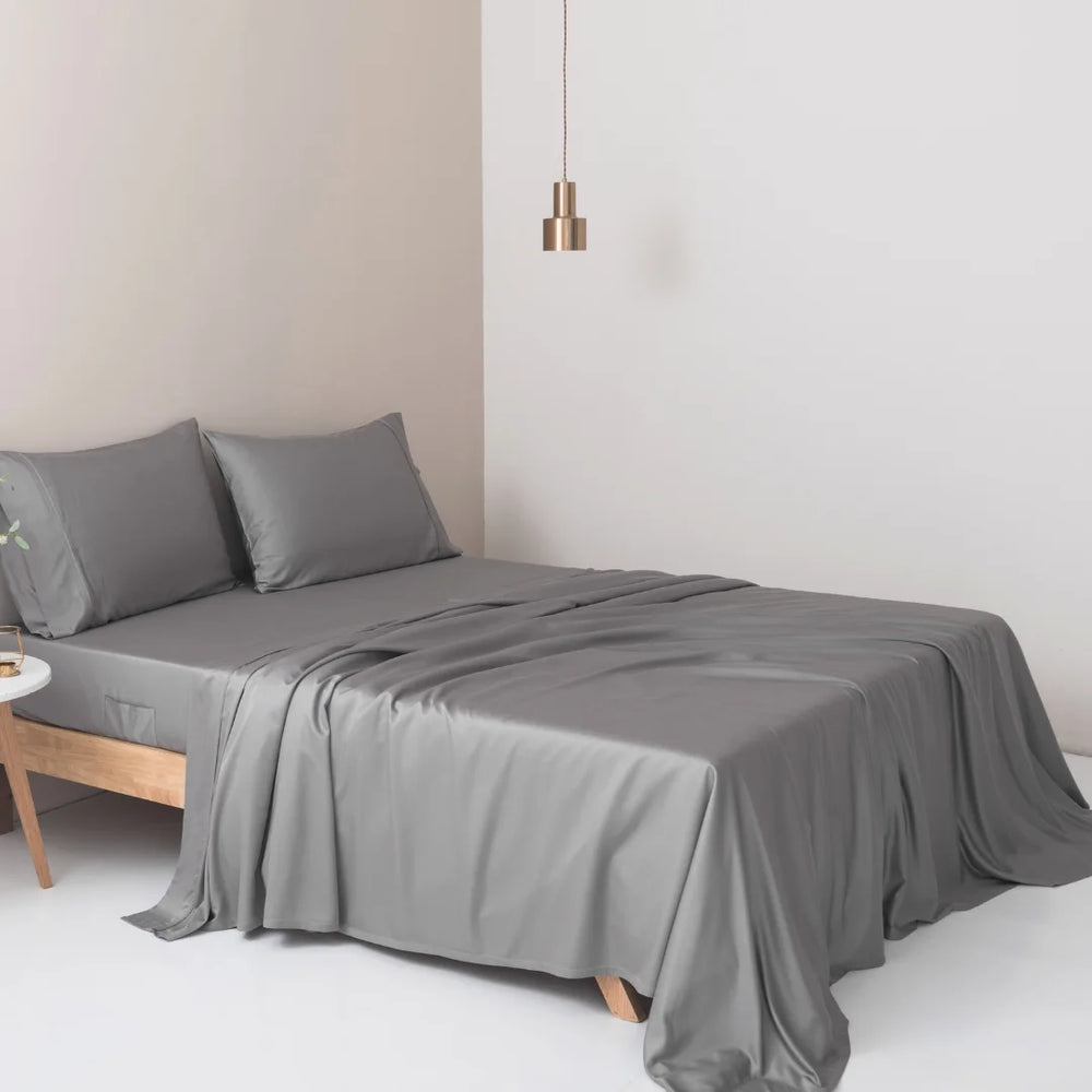 A minimalist bedroom with a neatly made bed featuring a Linenly Stone Grey bamboo sheet set, created from sustainable bamboo fibers, and a single pendant light hanging above.