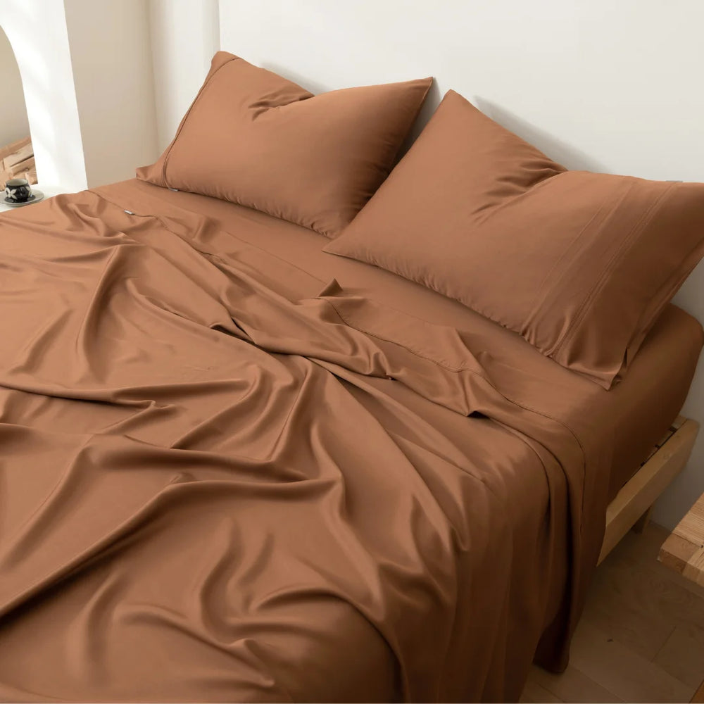 An unmade bed with crumpled Linenly Bamboo Sheet Set in Terracotta and pillows in a minimalist bedroom setting.