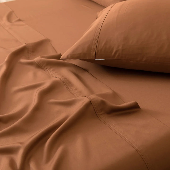 A close-up view of a neatly made bed with a smooth Linenly terracotta bamboo sheet set and a plush matching pillow, epitomizing stylish bedroom decor.