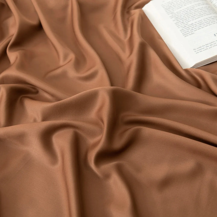 A book open atop Linenly's elegant, wavy terracotta Bamboo Sheet Set, suggesting a cozy reading session with a touch of luxury.