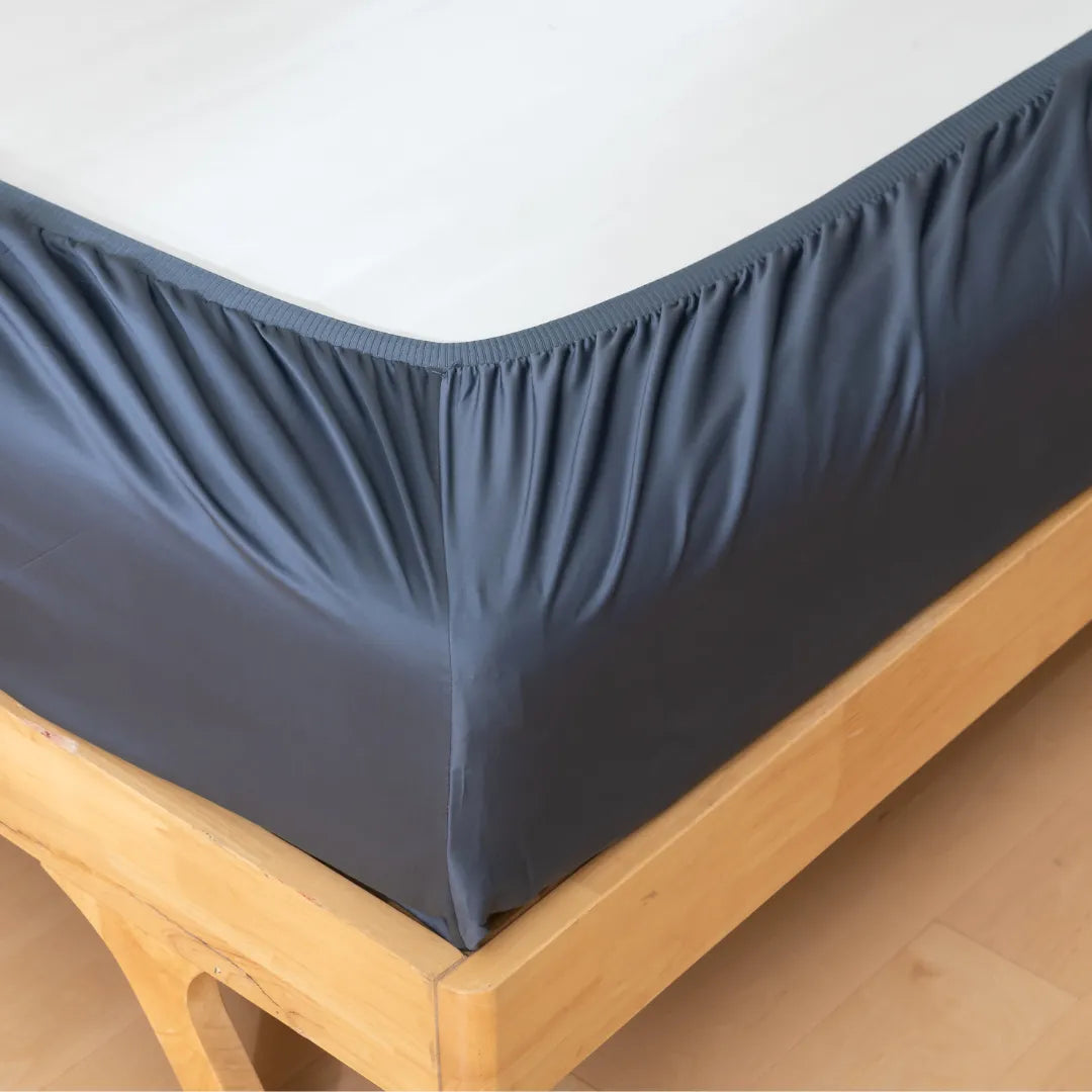 Crisp, dark gray bed skirt neatly draped over a wooden bed frame, complementing a clean, white mattress top with a Linenly Luxe Sateen Fitted Sheet in Midnight ensuring ultimate comfort.
