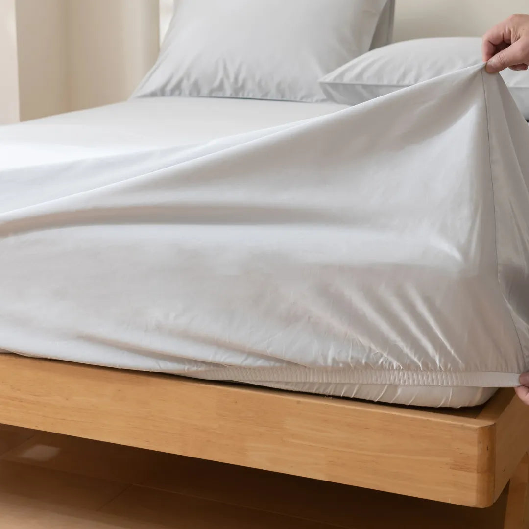 A person making the bed by neatly tucking a Linenly Luxe Sateen Fitted Sheet - Silver around the corner of a mattress.