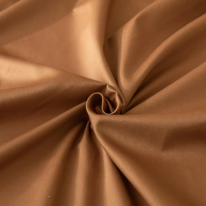 A close-up view of a Linenly Luxe Sateen Fitted Sheet in Terracotta color, elegantly twisted into a swirl, highlighting its smooth texture and sumptuous drape.