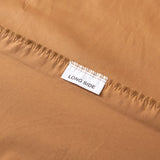 A close-up of Linenly’s Luxe Cotton Sateen Fitted Sheet in terracotta shows a “LONG SIDE” label stitched into the seam, highlighting this cozy bedding essential.