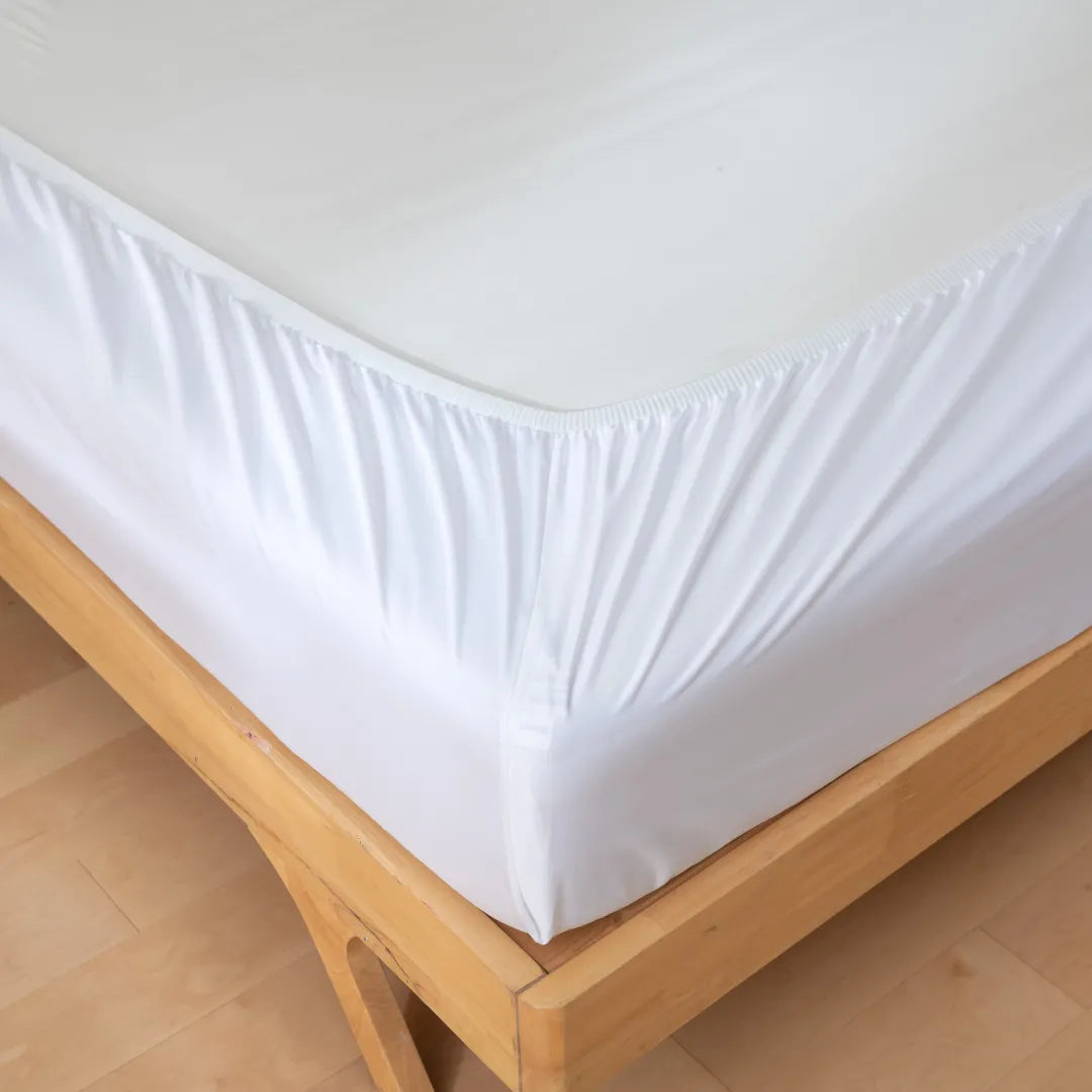 A neatly made bed with Linenly Luxe Sateen Fitted Sheet in white on a wooden bed frame.