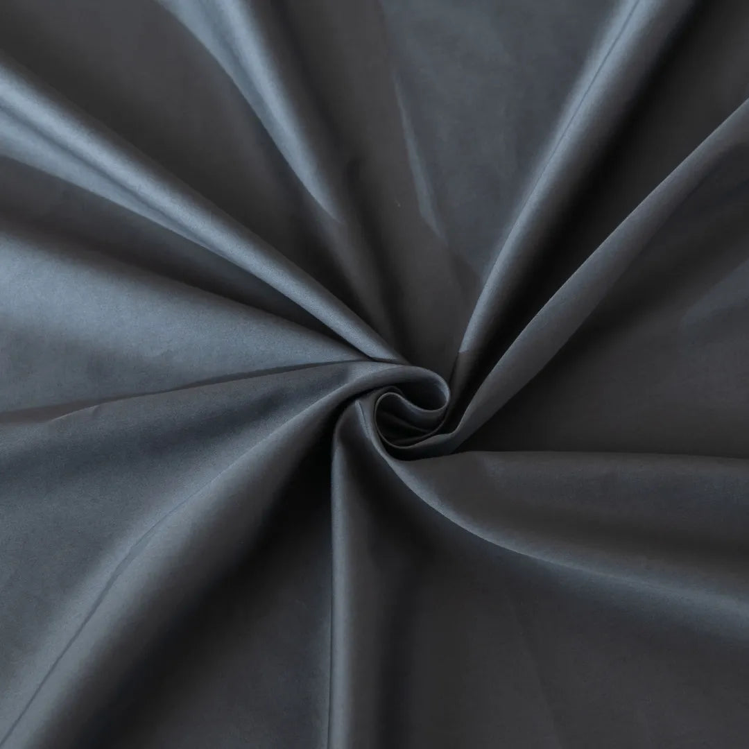 A close-up of a Linenly Luxe Sateen Flat Sheet in Charcoal, creating an elegant swirl pattern with soft light reflecting off its smooth, sateen weave surface.