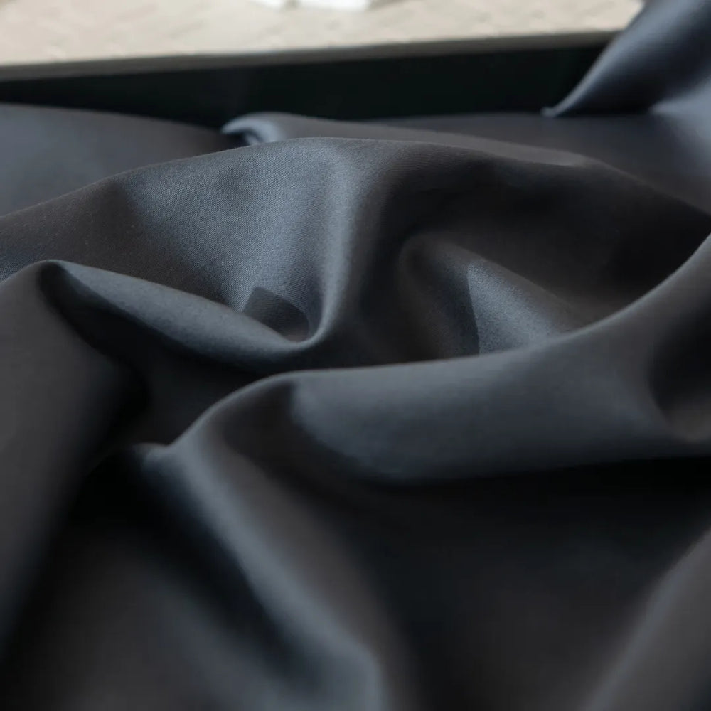 Luxe Sateen Charcoal Flat Sheet by Linenly, with soft folds placed inside a container, giving off an elegant and smooth appearance.