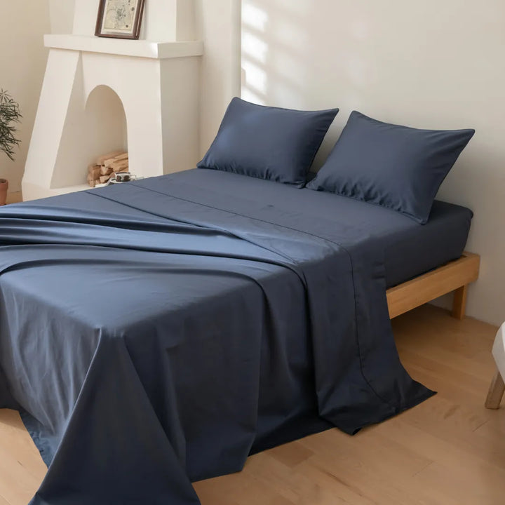 A neatly made bed with Linenly's Luxe Sateen Flat Sheet - Midnight, 500 thread count premium long staple cotton bed linens in a bright, minimalist bedroom.